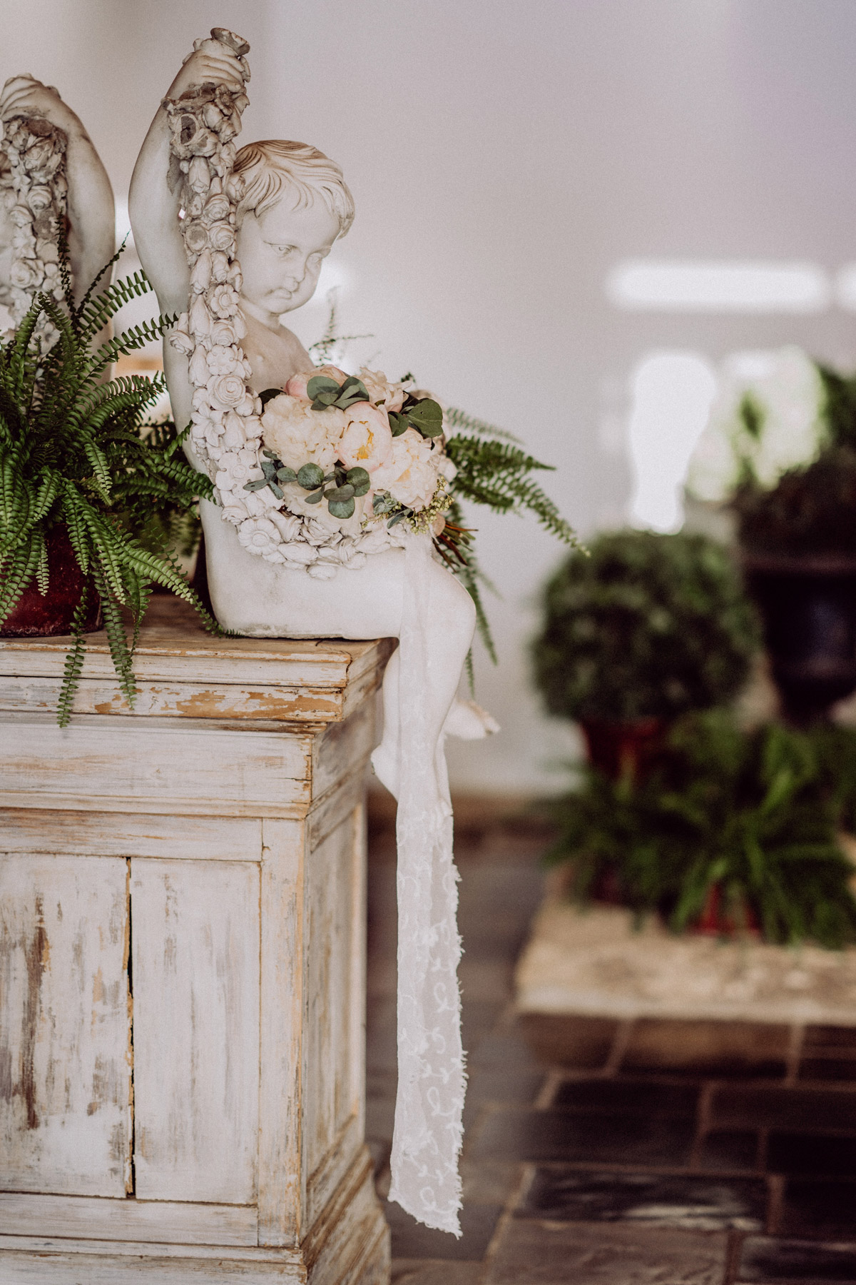 Brautstrauß mit blassrosa Pfingstrosen und Eukalyptus liegt auf Statue