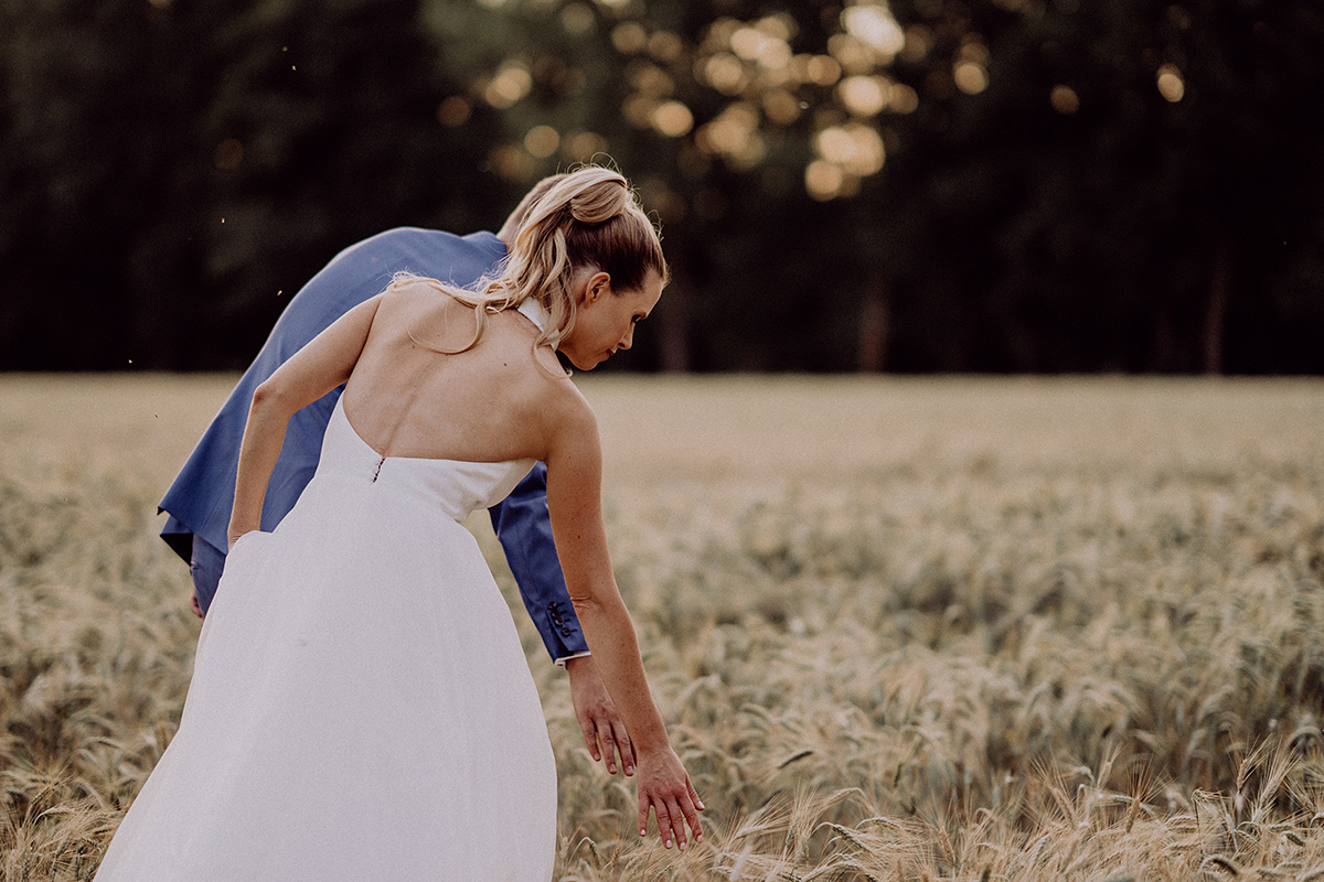 Brautpaarfoto von hinten: Braut streicht über Ähren des Feldes