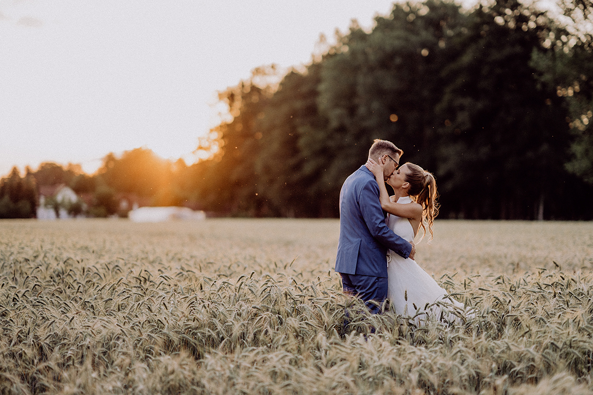 Paarshooting Bleiche Hochzeit: Paar küsst sich bei Sonnenuntergang vor einem Wald