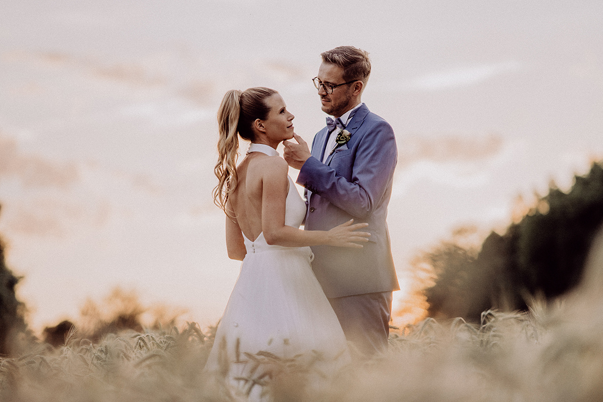 Spreewald Hochzeitsfotografie: Brautpaar steht im Sonnenuntergangslicht auf Feld mit Wald im Hintergrund