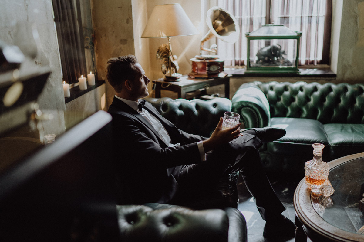 Bräutigam entspannt mit Drink in der Bar des The Grand Berlin: Stilvolle Hochzeitsfotos im Vintage-Look