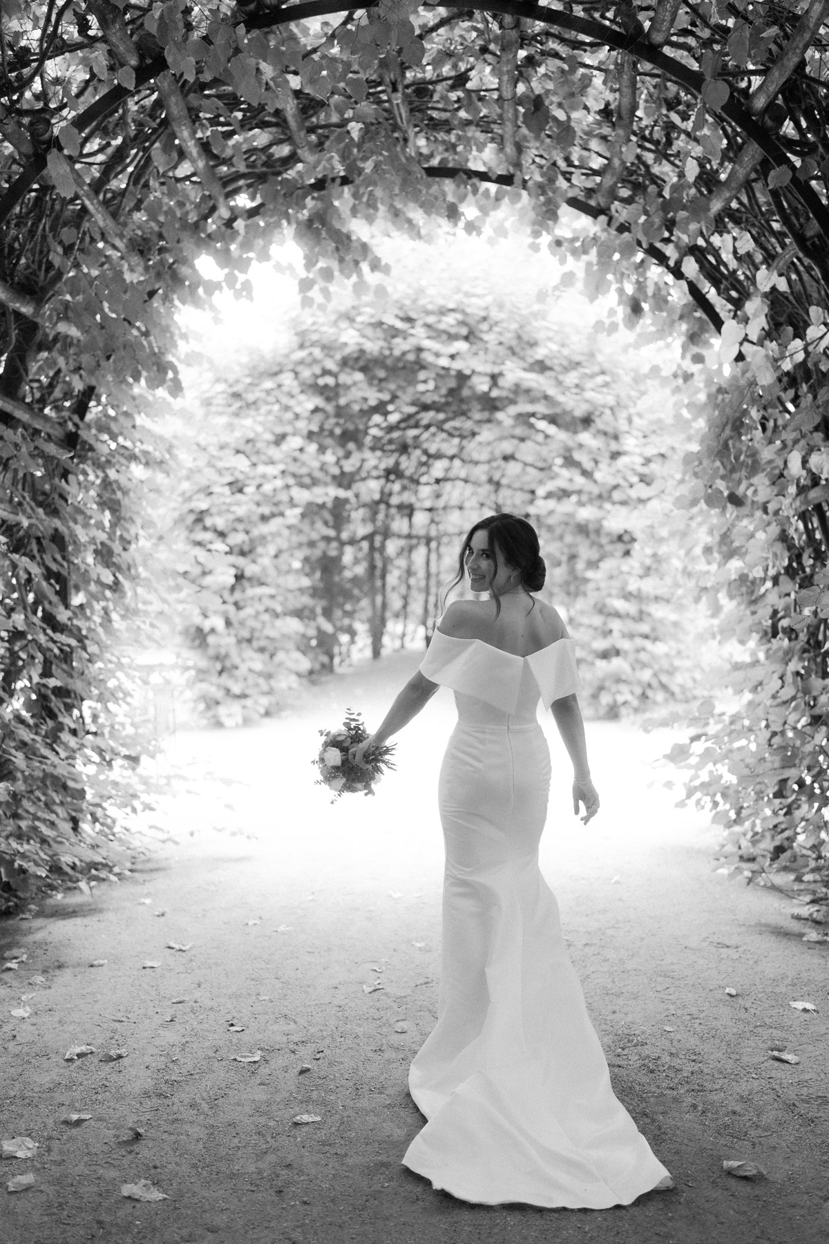 Braut geht unter grünen Blätterbogen zum Schloss Belvedere und schaut über die Schulter