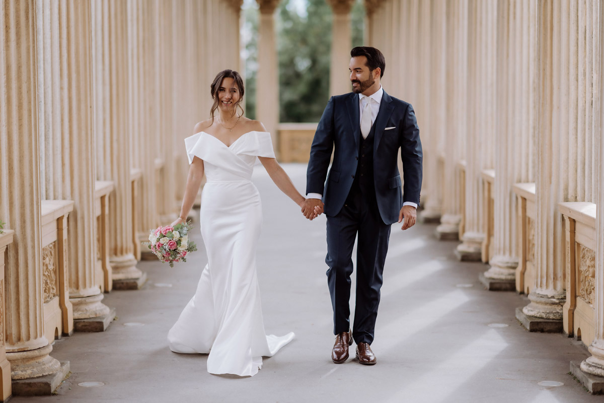 Brautpaar läuft Hand in Hand im Säulengang zum Standesamt Potsdam