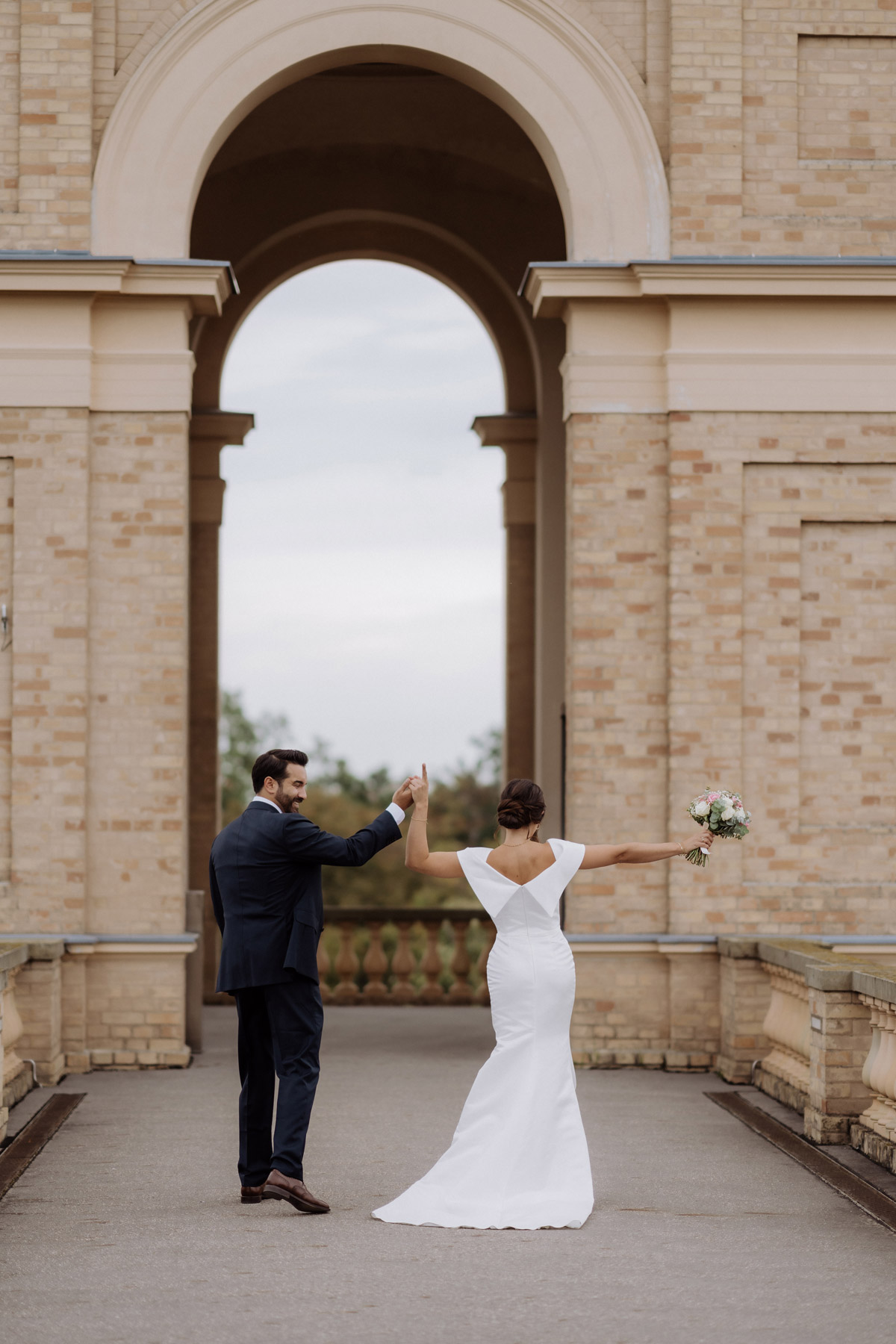 Fotoshooting Brautpaar von hinten feiert unter Rundbogen vom Schloss Belvedere auf dem Pfingstberg