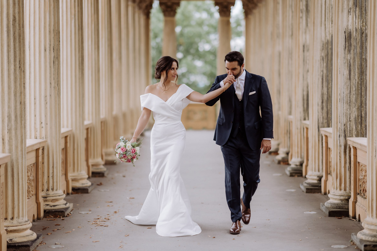 Bräutigam küsst Braut während des Gangs durch die Kolonnaden auf die Hand