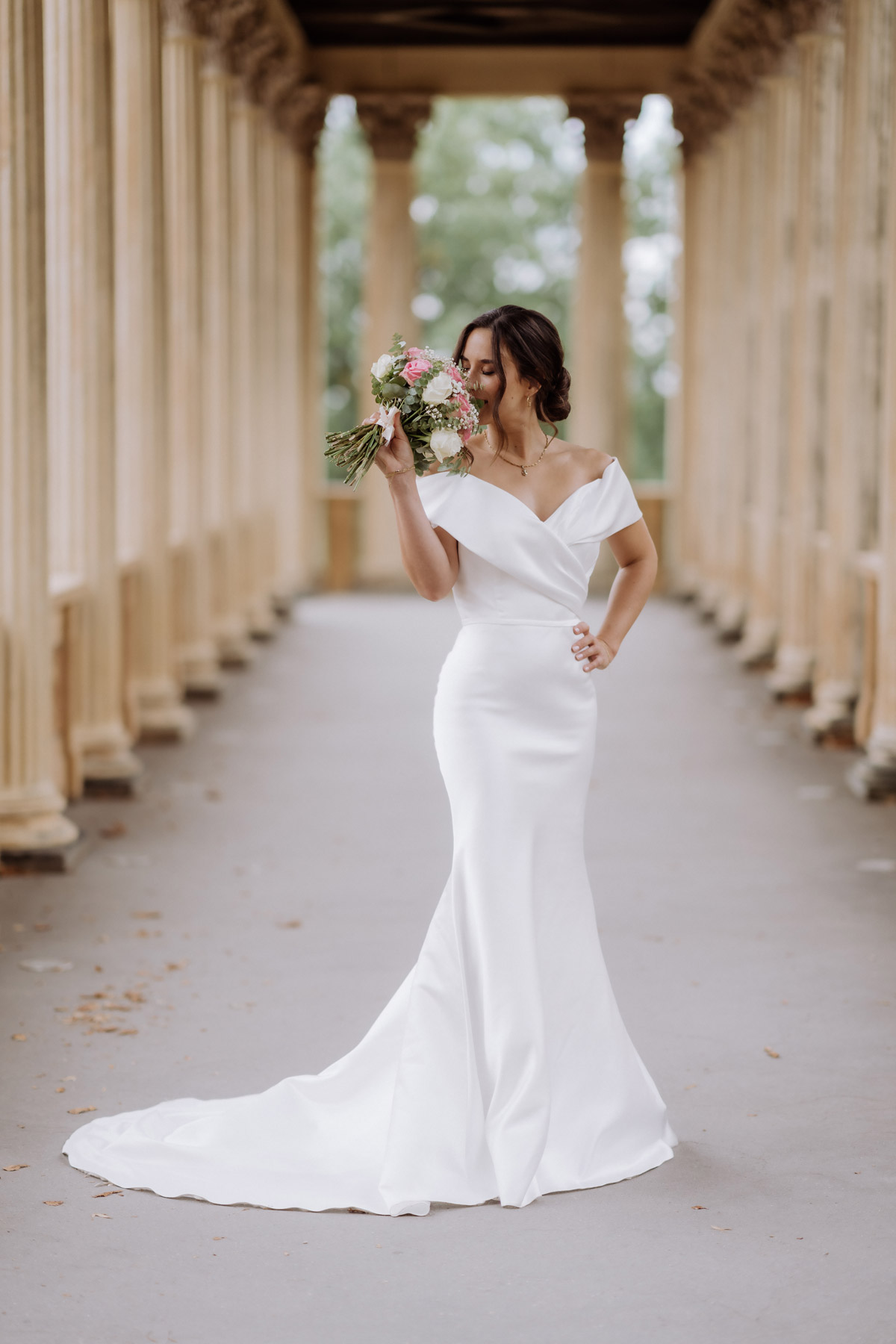 Braut riecht am Brautstrauß in den Kollonaden vom Schloss Pfingstberg