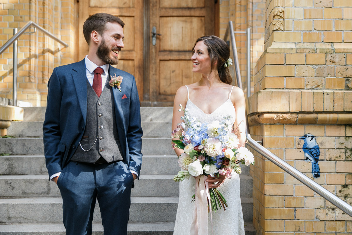 Urbane Hochzeitsfotos im Berliner Kiez: Bräutigam blickt verliebt zu seiner Braut auf der Treppe eines historischen Backsteingebäudes