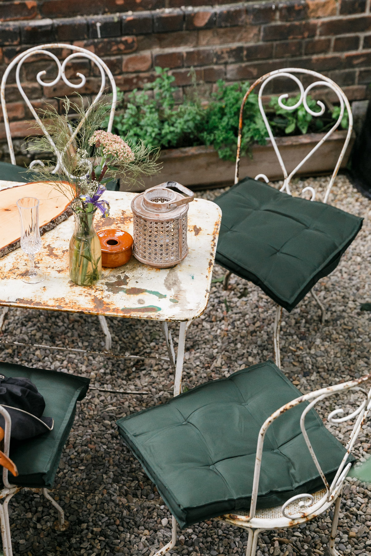 Vintage-Hochzeitsdeko in Berlin: Rustikaler Tisch mit Gartenstühlen und zarten Wiesenblumen im idyllischen Hinterhof der Alten Schmiede