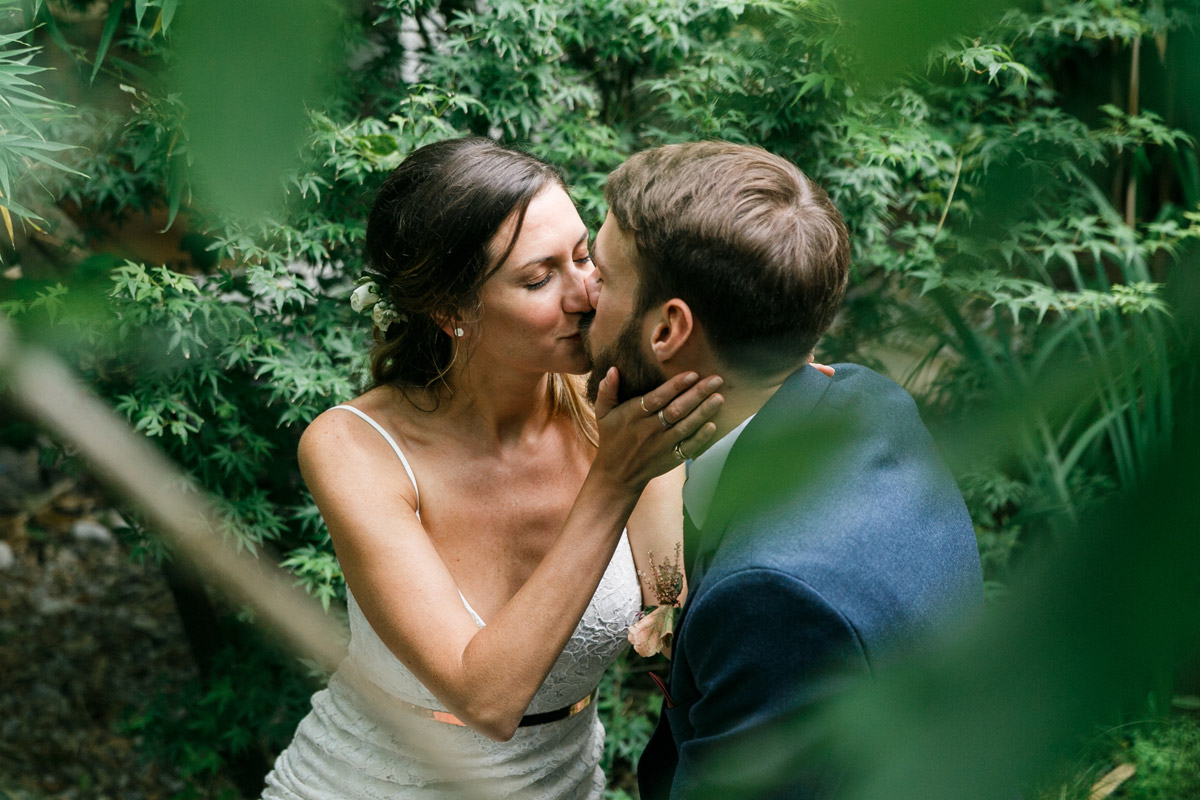 Brautpaar küsst sich versteckt im Grünen