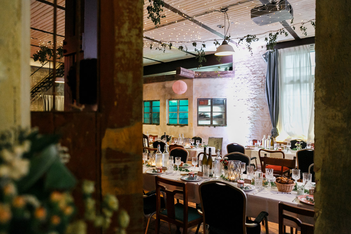 Urbane Hochzeitslocation Berlin Friedrichshain: Versteckter Blick durch den Türrahmen in den festlich beleuchteten Speisesaal des Old Smithy's Dizzle