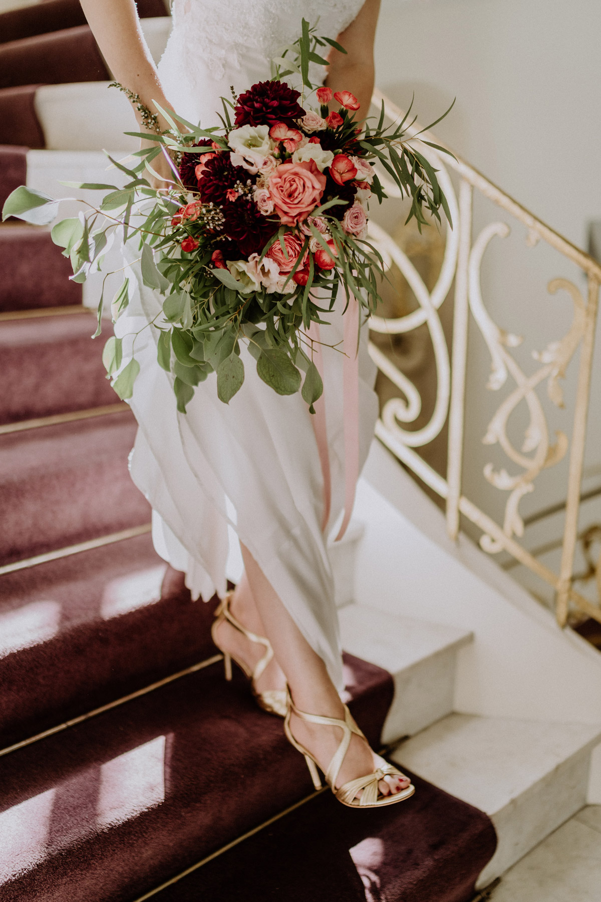 Stilvolle Hochzeitsdetails: Brautstrauß in Rot- und Rosatönen und elegante Riemchensandalen auf der Treppe des Standesamts Mitte