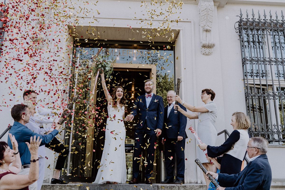 Hochzeitsfotograf Berlin Mitte: Jubelndes Brautpaar beim Auszug aus dem Standesamt Ermelerhaus im goldenen und roten Konfetti-Regen