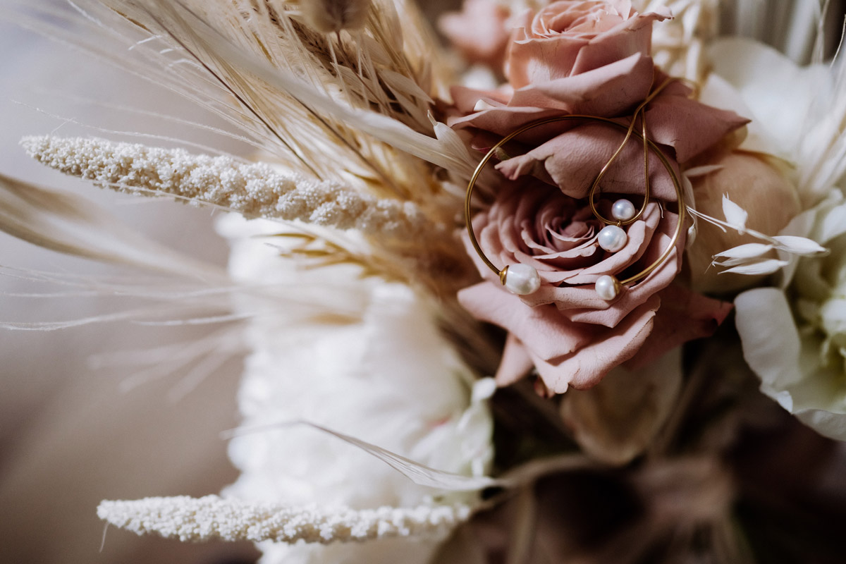 Moderner Brautschmuck in Gold mit Perlen liegt auf den Hochzeitsblumen