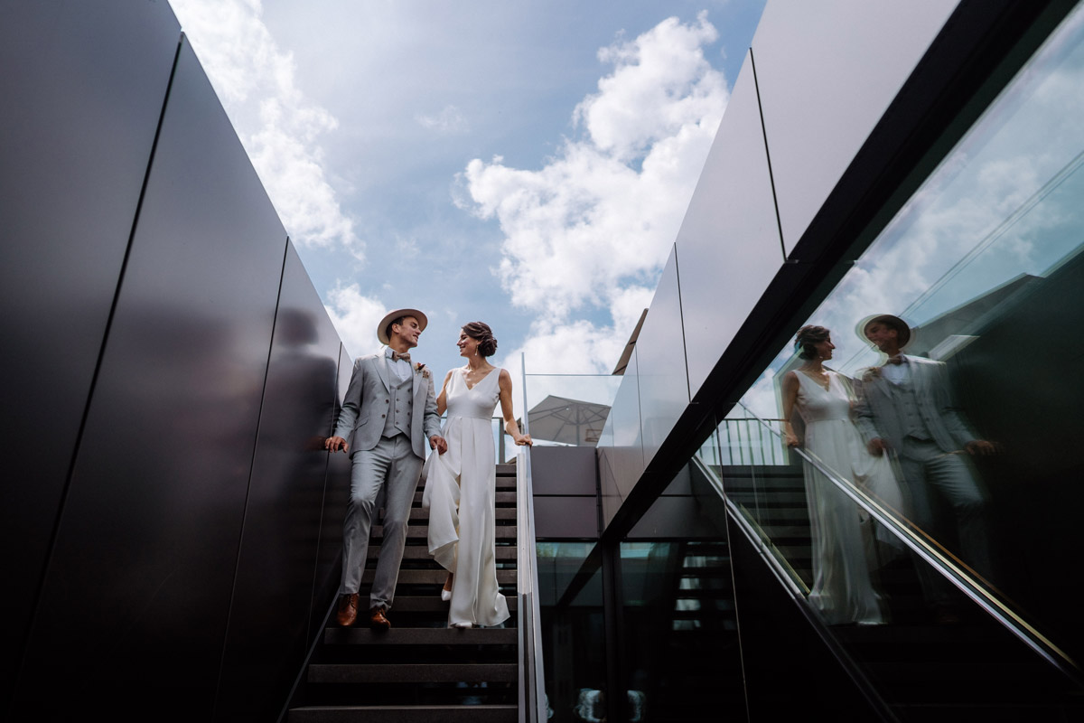 Modernes Elopement im KPM Hotel: Brautpaar läuft entspannt die Design-Treppe hinunter unter freiem Himmel