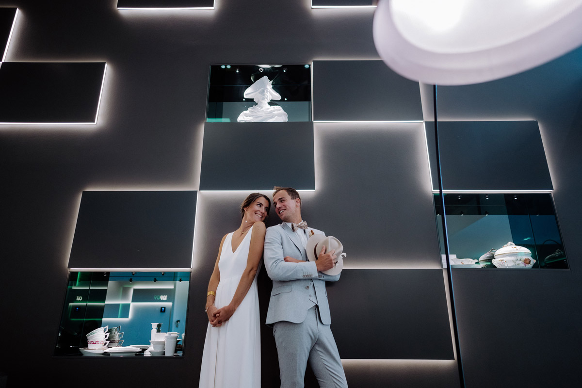 Exklusive Hochzeitsfotos im KPM Hotel Berlin: Brautpaar posiert lässig vor den beleuchteten Vitrinen