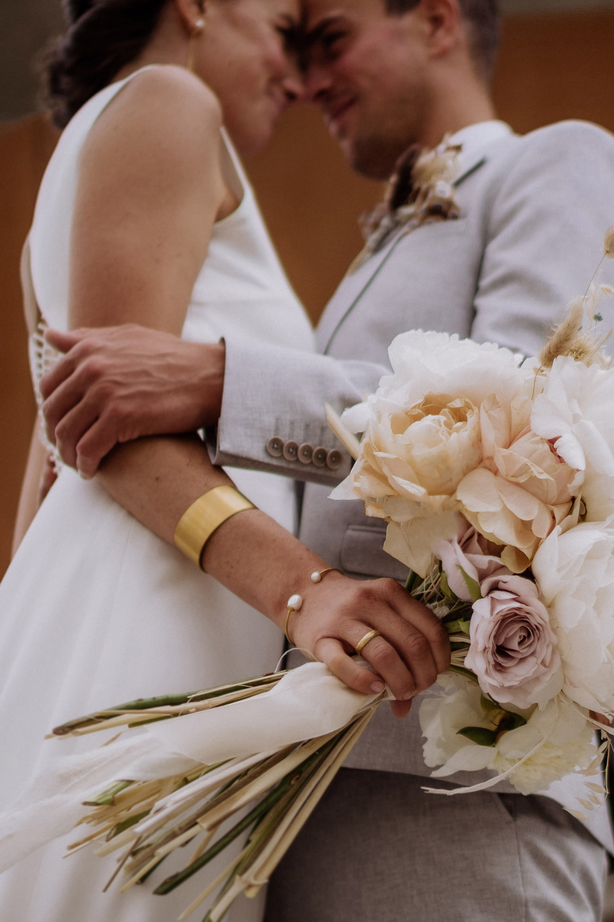 Kreative Detailaufnahme bei der Reportage: Brautstrauß und Brautschmuck mit Paar unscharf im Hintergrund