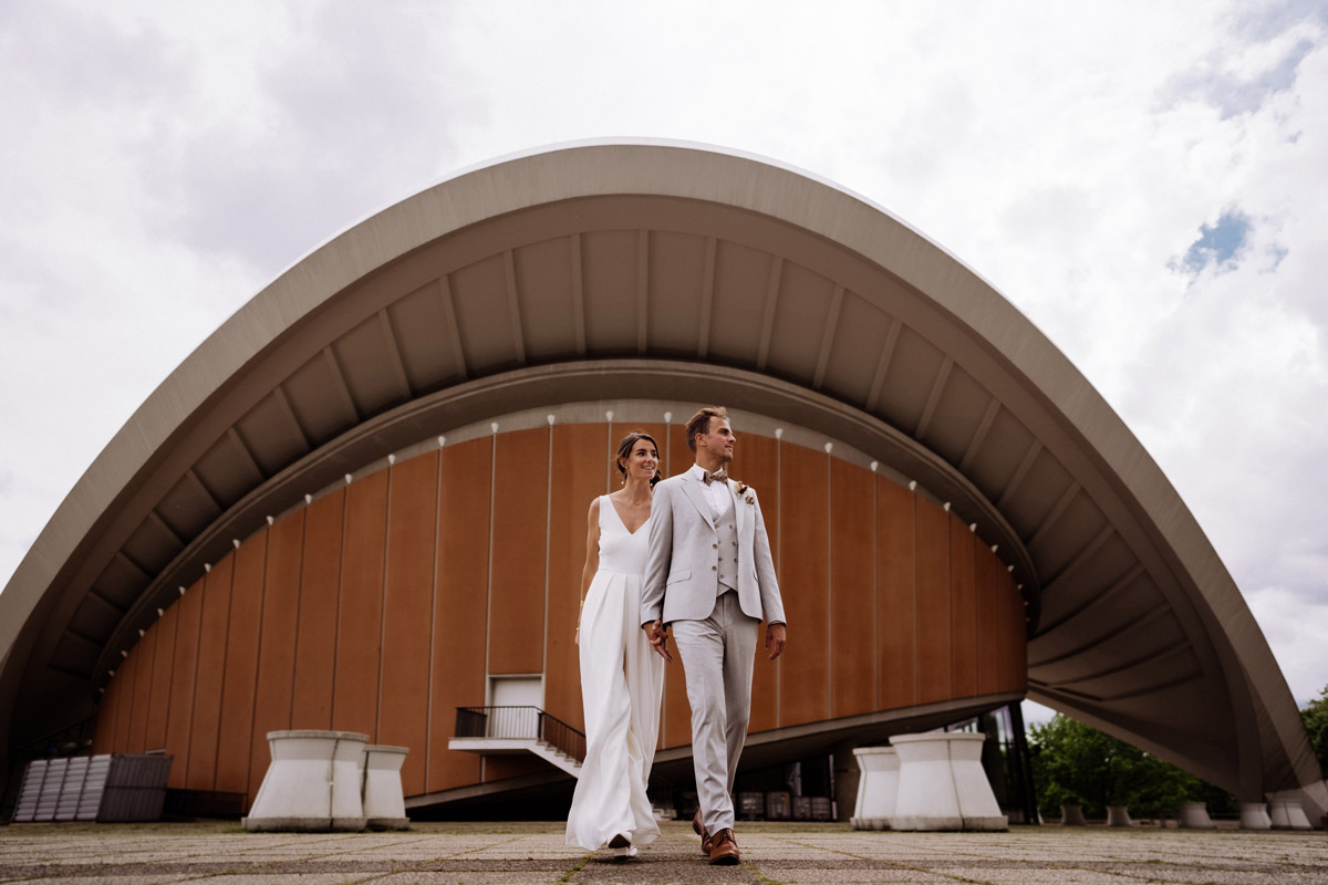 Imposante Hochzeitsfotos vor Berliner Architektur: Brautpaar spaziert entspannt vor der gigantischen Dachkonstruktion