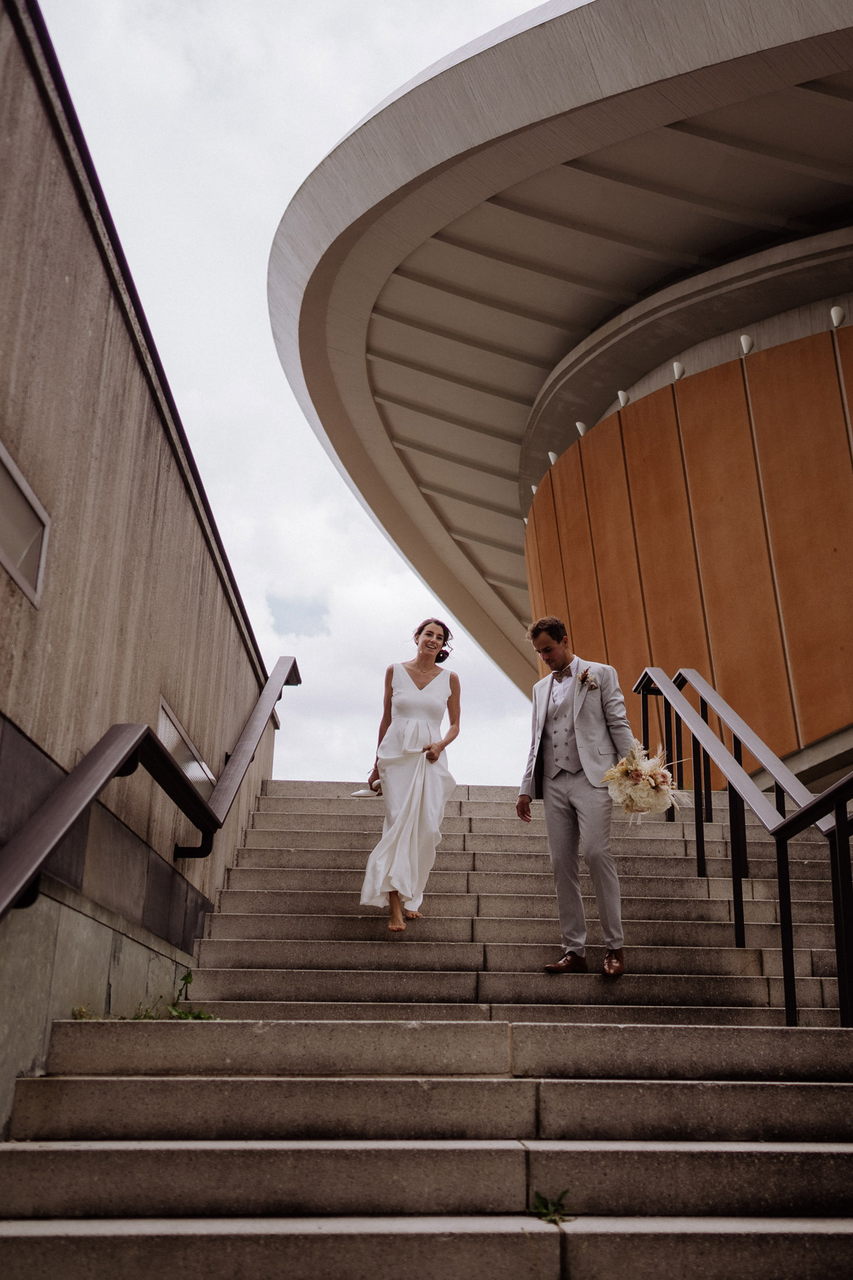 Entspannte Hochzeit in Berlin: Braut läuft barfuß mit Brautschuhen in der Hand die Treppe herunter