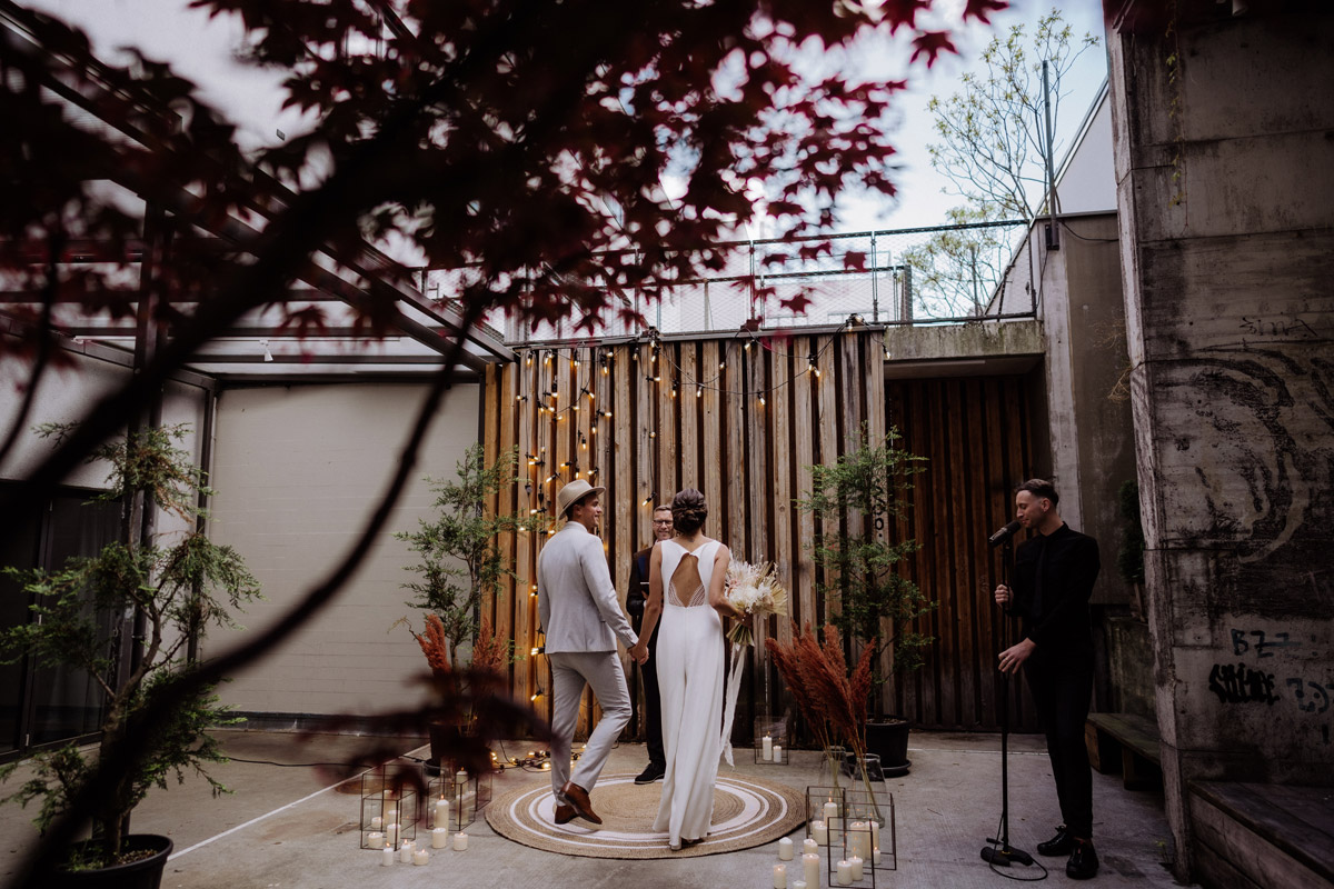 Intime freie Trauung im Innenhof: Emotionales Berlin Elopement vor modernem Holz-Backdrop mit Lichterketten