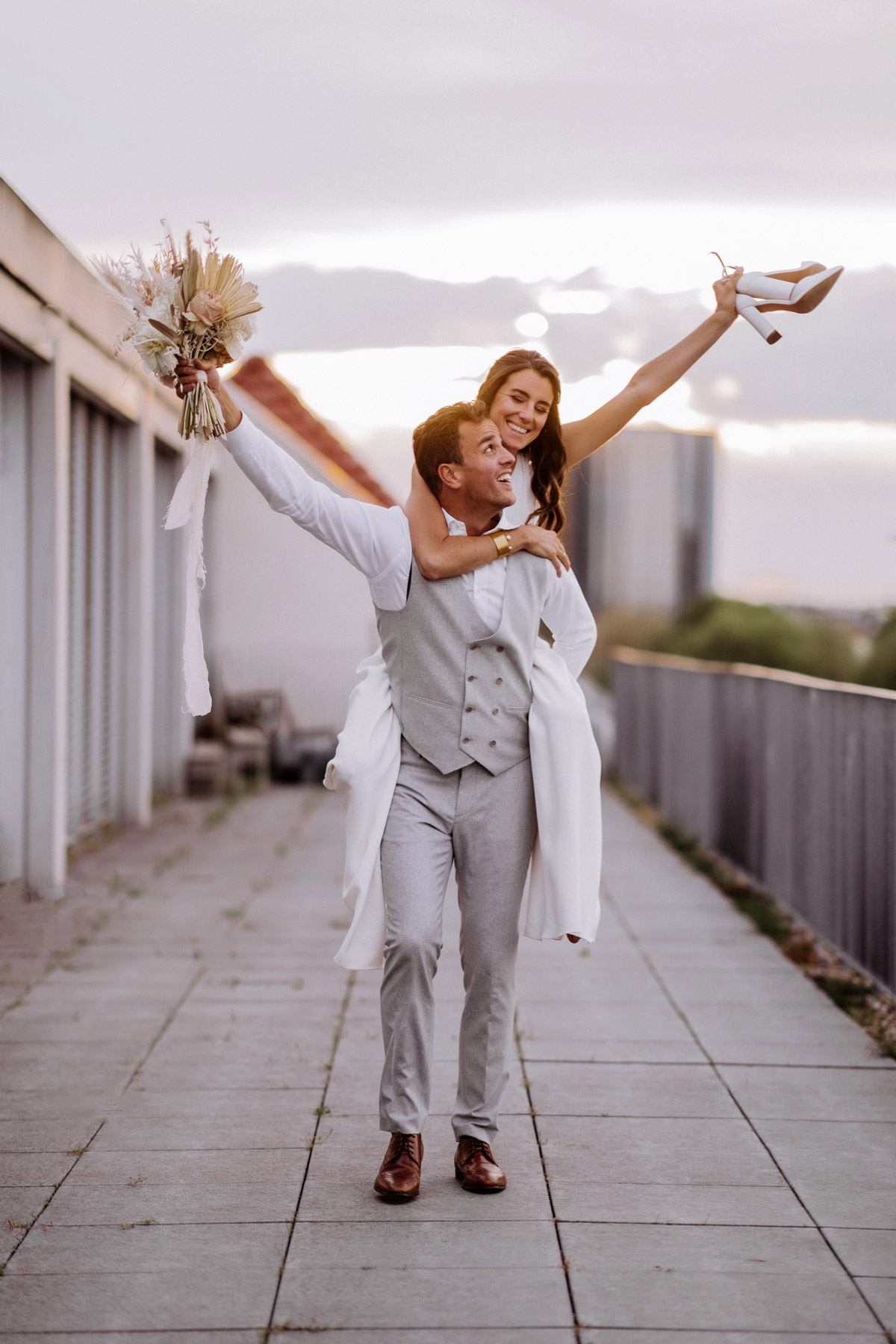 Ausgelassene Stimmung nach der Trauung: Bräutigam trägt Braut huckepack, während sie die Brautschuhe in die Luft hält