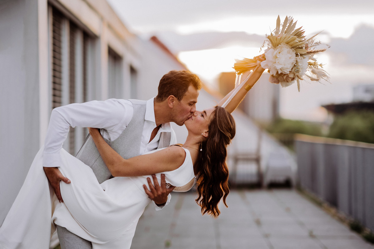 Leidenschaftlicher Kuss im Sonnenuntergang: Dynamisches Posing beim Brautpaar-Shooting auf der Berliner Dachterrasse