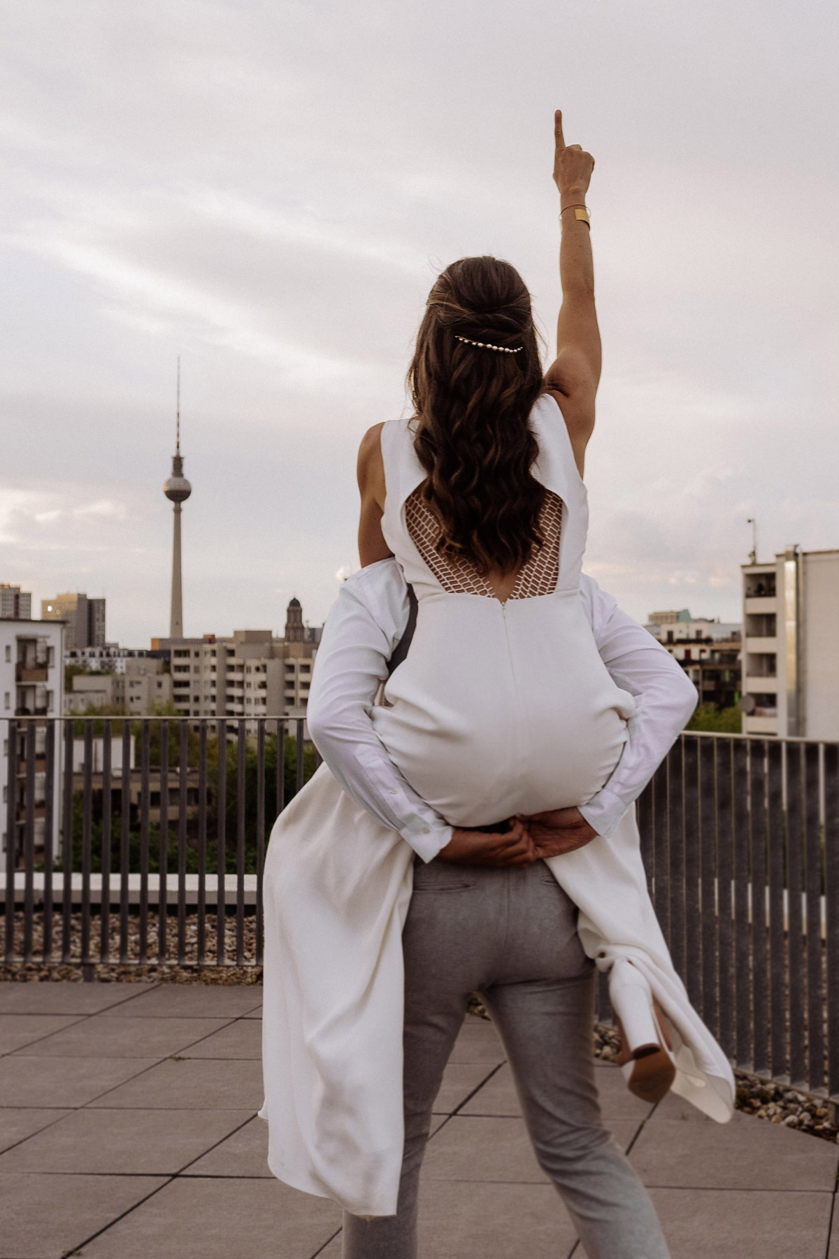 Hochzeitsfotos mit Wahrzeichen: Braut auf dem Rücken des Bräutigams zeigt begeistert zum Berliner Fernsehturm