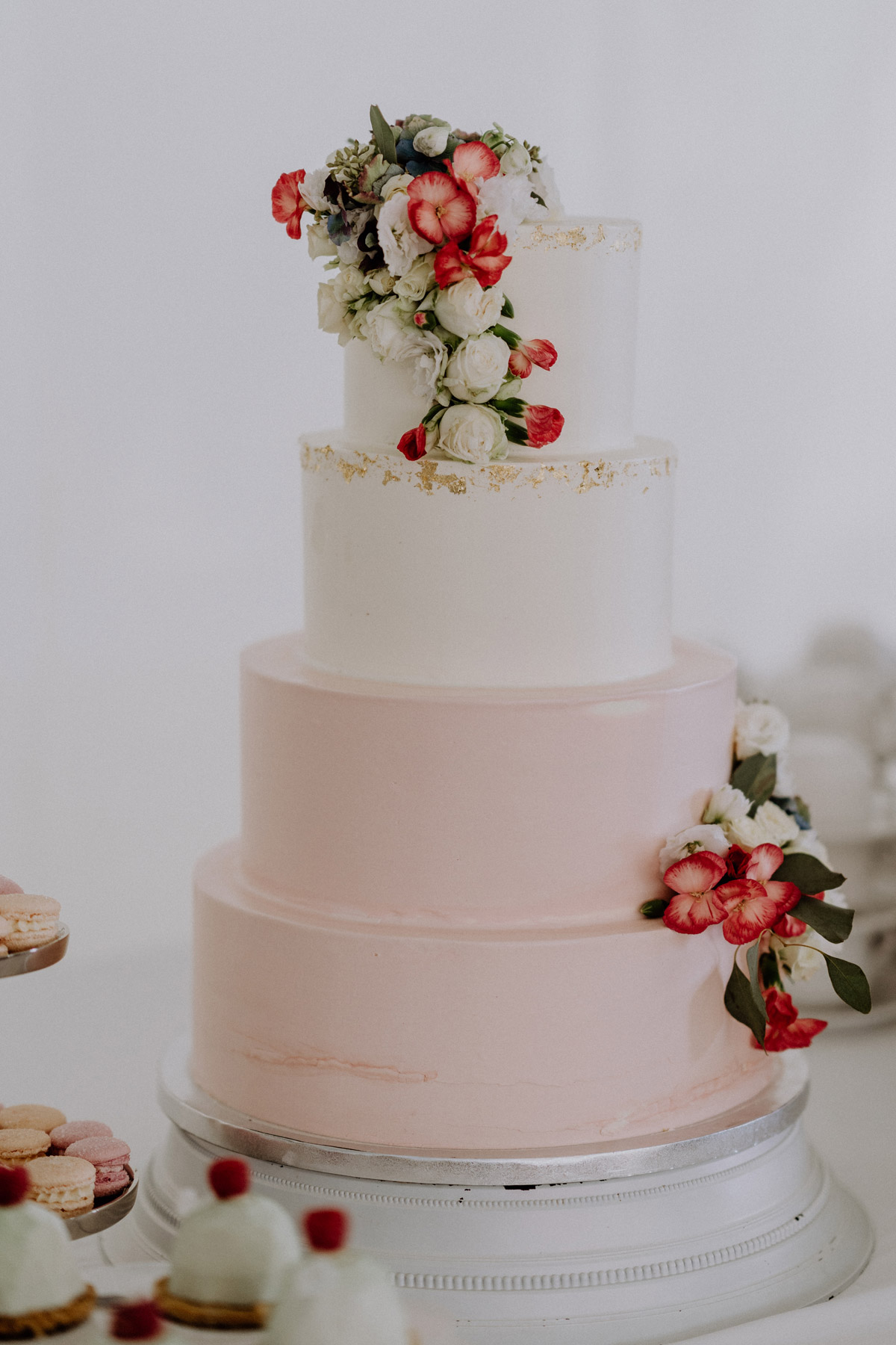 Dreistöckige Hochzeitstorte in Weiß und Zartrosa, stilvoll dekoriert mit frischen Blumen auf dem Sweet Table