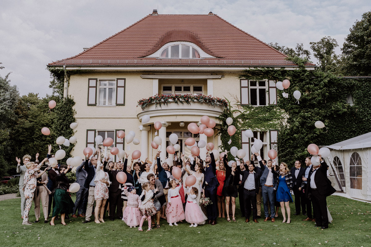Gut Schloss Golm Hochzeit: Außenaufnahme der Hochzeitsgesellschaft beim gemeinsamen Steigenlassen von Luftballons vor dem Schloss