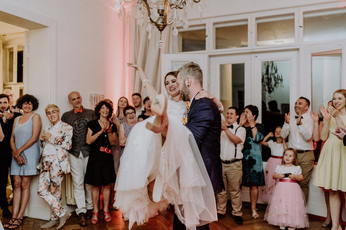 Hochzeitsfeier auf Gut Schloss Golm: Ausgelassener Hochzeitstanz im Festsaal, Bräutigam hebt seine Braut jubelnd unter dem Kronleuchter hoch