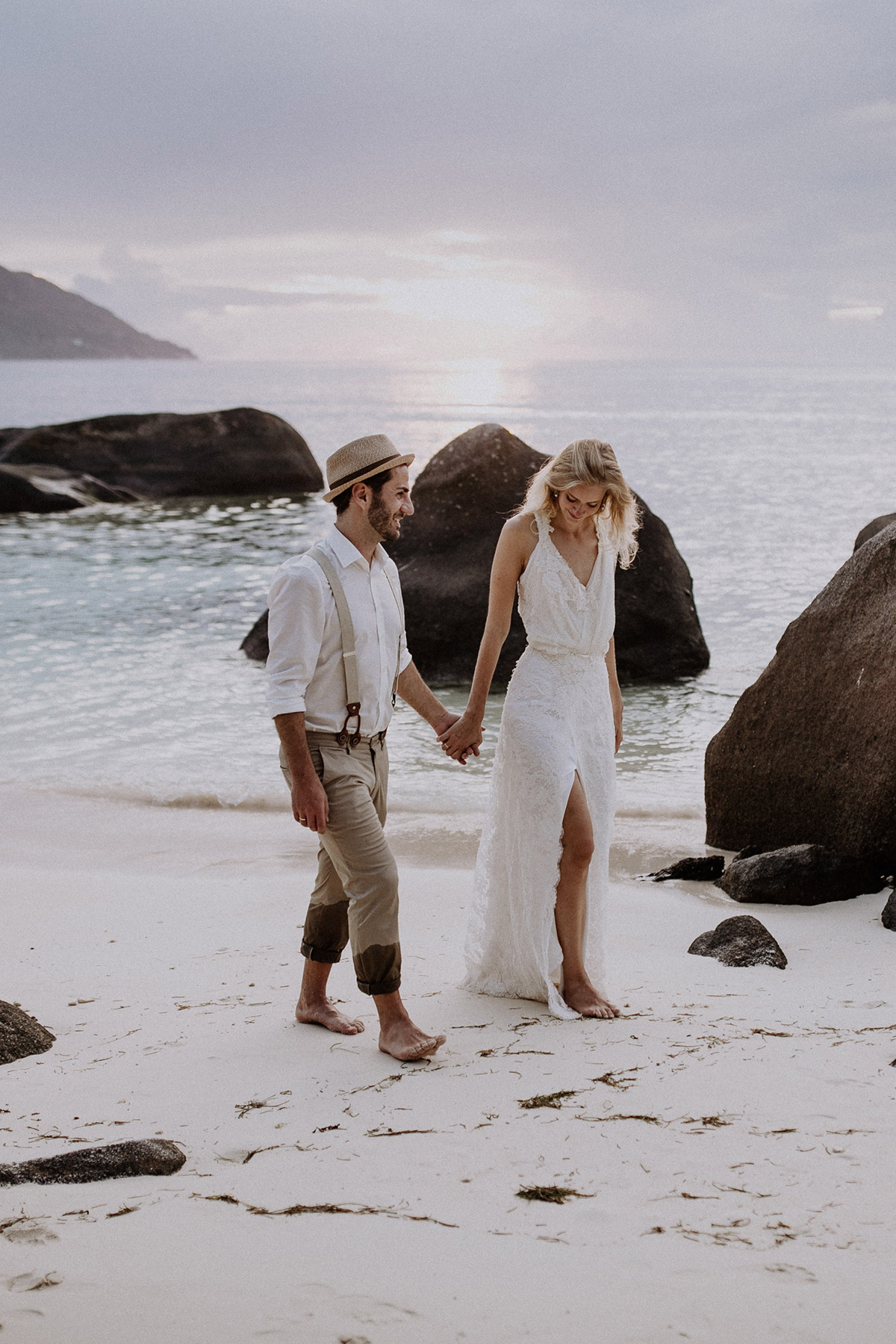 Heiraten im Ausland: Das glückliche Paar spaziert nach dem Berliner Standesamt barfuß und händehaltend entlang der beeindruckenden Granitfelsen am tropischen Strand