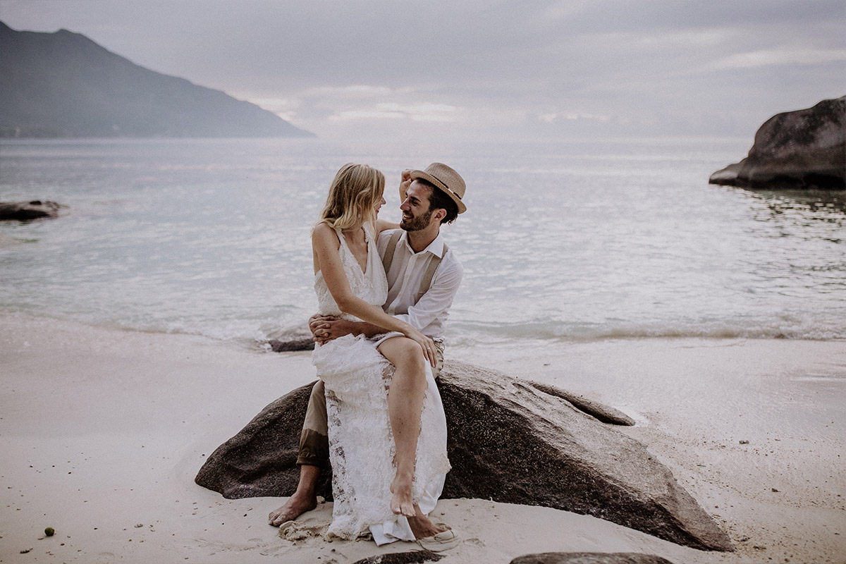 Heiraten in Charlottenburg und weltweit: Romantisches Brautpaarfoto auf einem typischen Granitfelsen am Meer der Seychellen als krönender Abschluss nach dem Berliner Standesamt