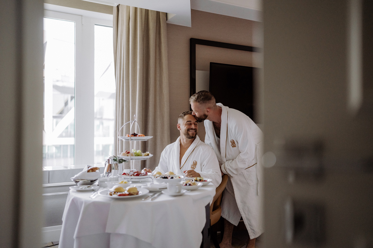 Entspanntes Getting Ready im Ritz-Carlton Berlin: Bräutigam küsst Partner zum Frühstück auf die Stirn