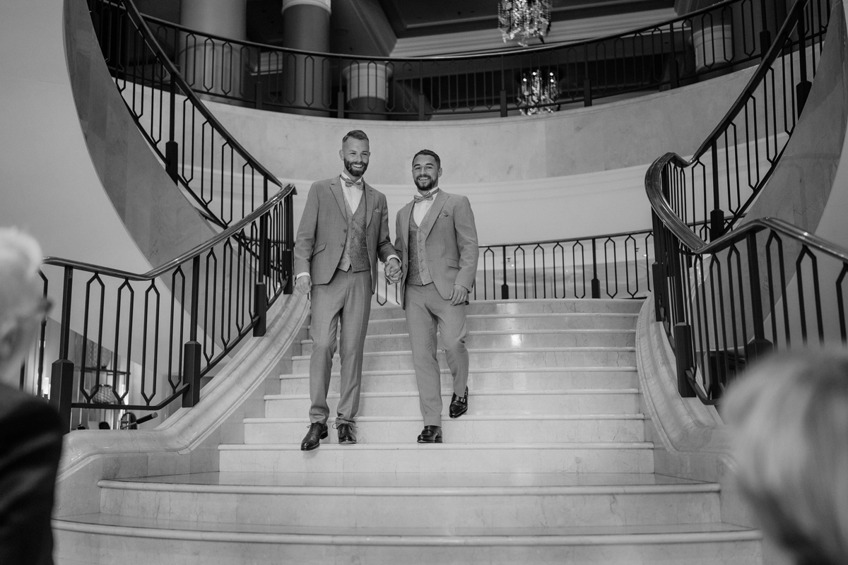 Bräutigame schreiten Hand in Hand die große Treppe im Ritz-Carlton Berlin hinab