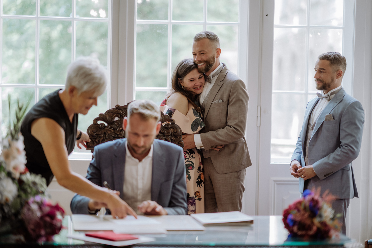 Hochzeitspaar umarmt Trauzeugin während der Unterschrift