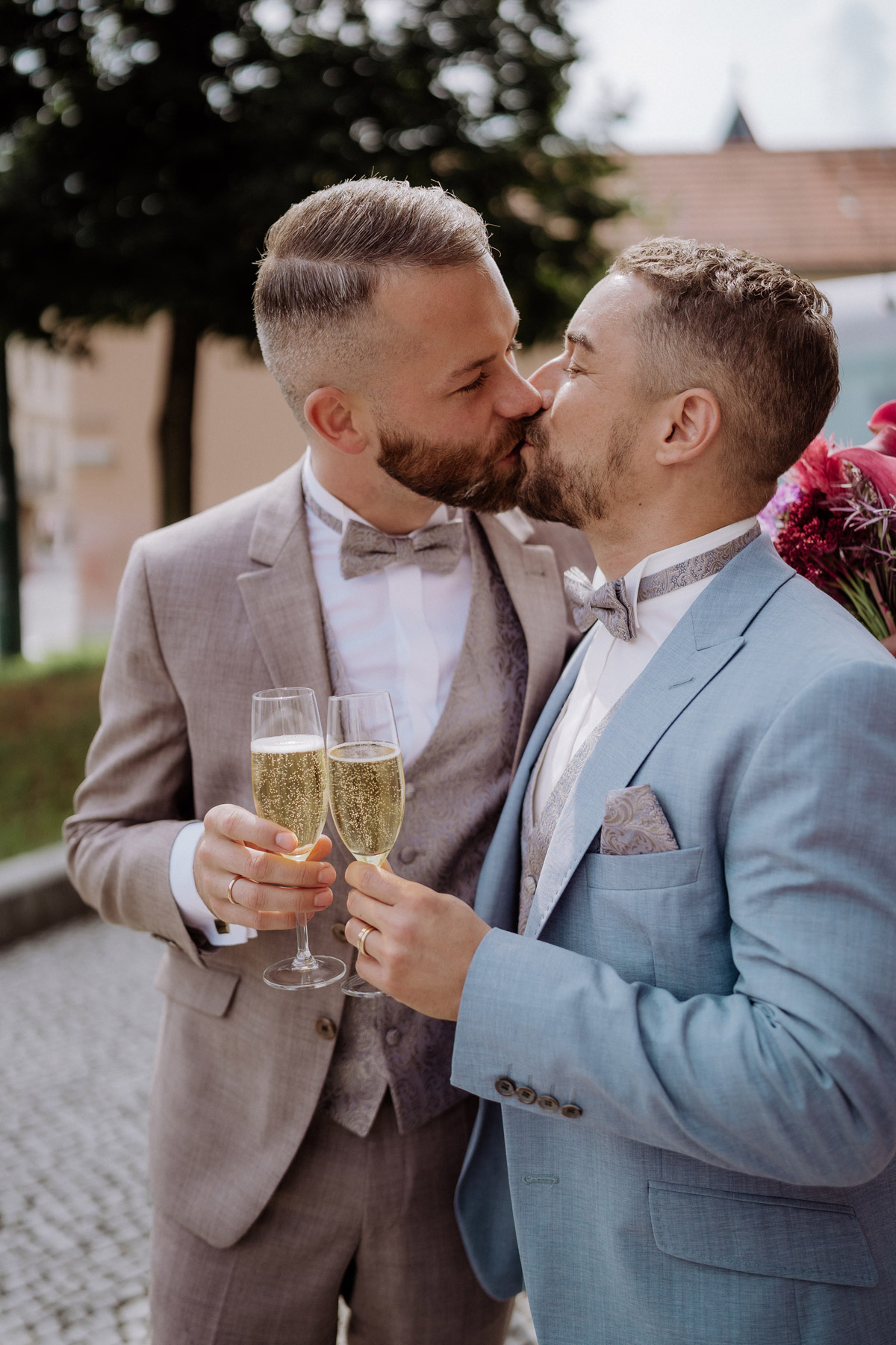 männliches Hochzeitspaar küsst sich mit Sekt in der Hand