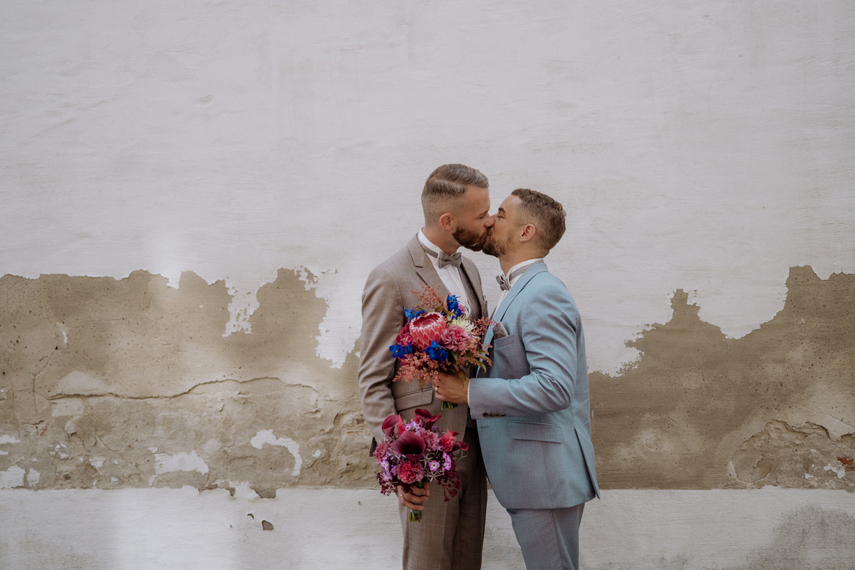 Gleichgeschlechtliche Hochzeit: Kuss des Paares mit Blumensträußen in der Hand