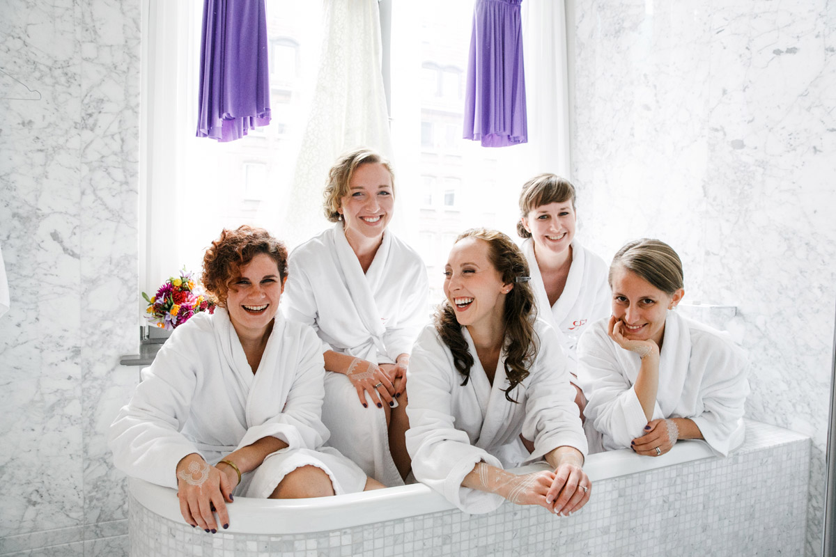 Spaß mit den Brautjungfern: Braut und ihre Freundinnen lachen entspannt in Bademänteln in der Badewanne des Hotel de Rome – Getting Ready Fotos