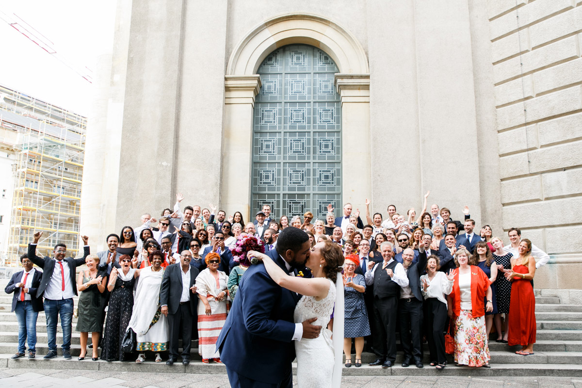 Fröhliches Gruppenfoto der gesamten Hochzeitsgesellschaft: Internationale Gäste jubeln dem Brautpaar zu – Hochzeitsfotograf Berlin