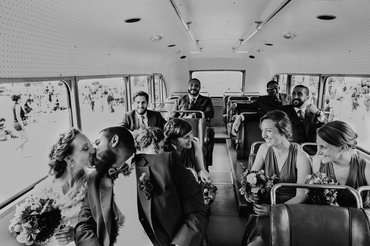 Brautpaar küsst sich im Bus und Gäste lachen auf den Bänken