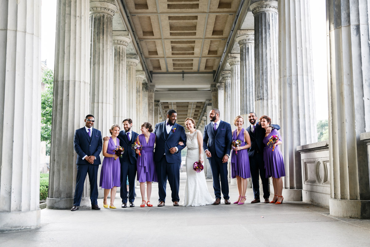 Klassisches Gruppenfoto der Hochzeitsgesellschaft im Säulengang auf der Museumsinsel: Brautpaar lacht mit Freunden