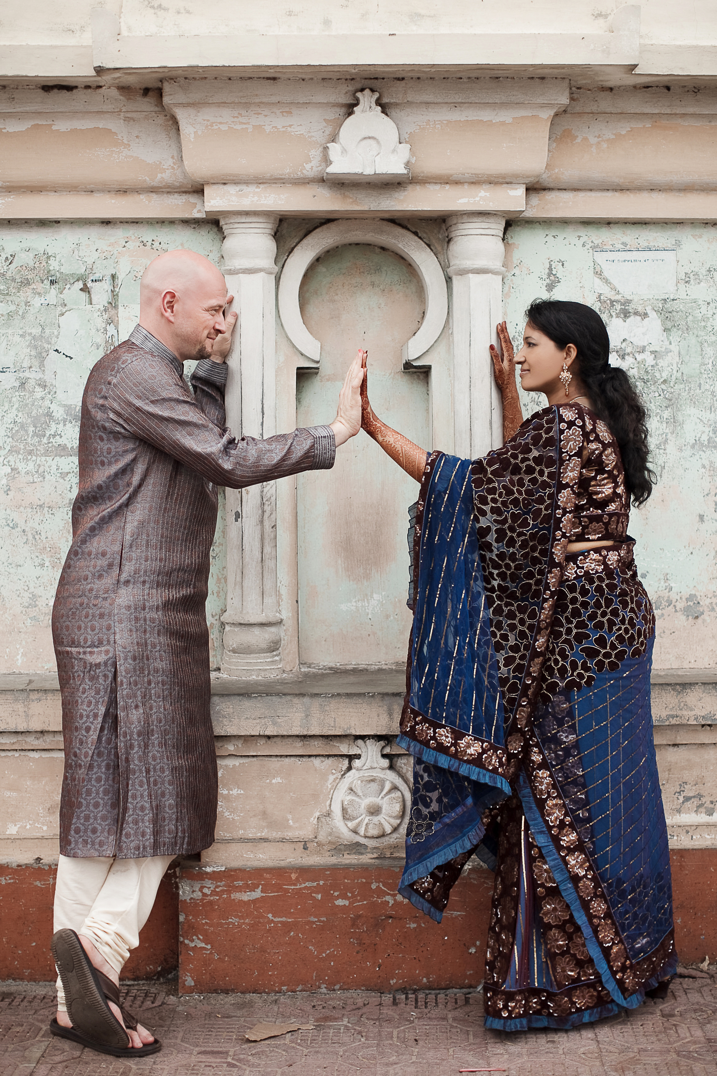 Destination Wedding Photographer: Braut und Bräutigam berühren sich an den Händen vor einer historischen Wandkulisse in Indien