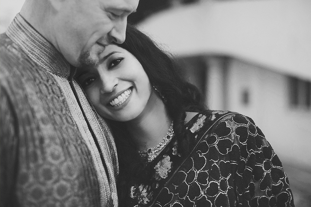 Indian Wedding Photography: Glückliche Braut lehnt sich beim romantischen Paarshooting vertraut an ihren Bräutigam (Schwarz-Weiß)