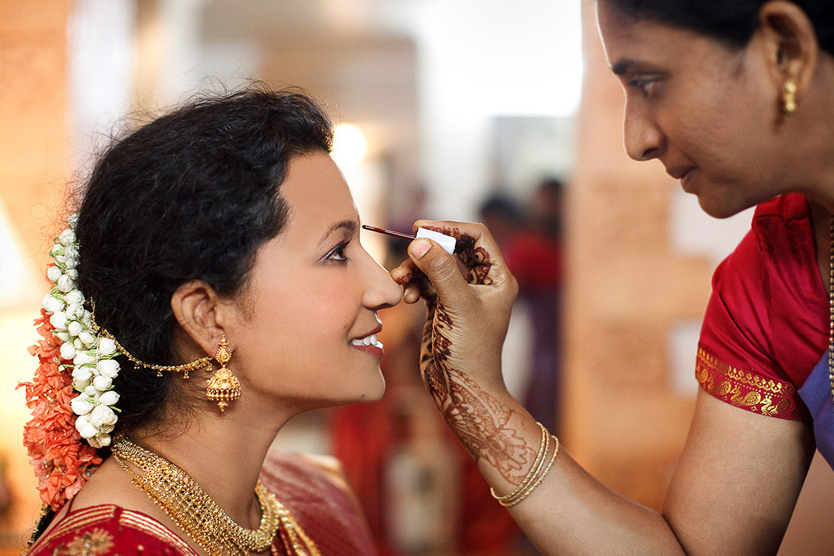Fotograf indische Hochzeit: Traditionelles Getting Ready der Braut, der das rote Bindi auf die Stirn aufgetragen wird