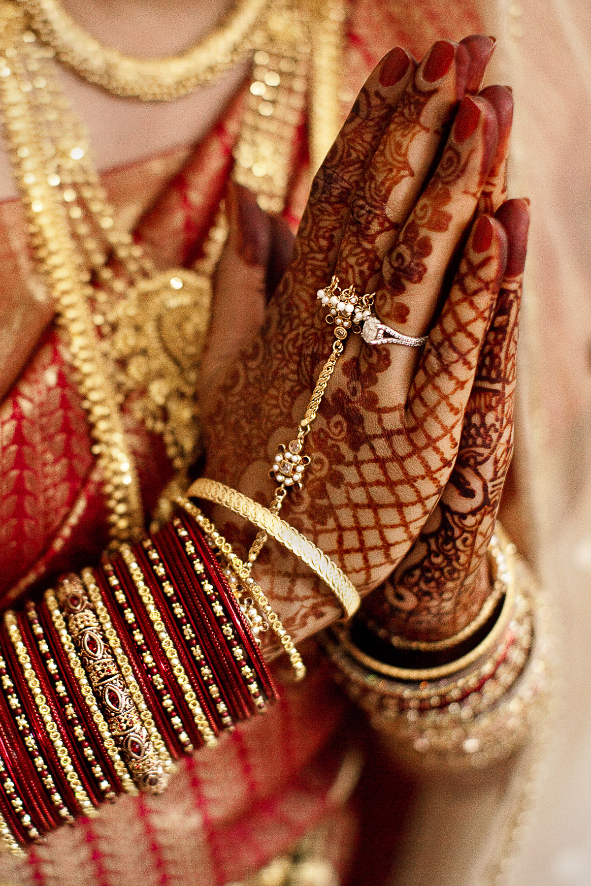 Hindu Wedding Photographer Berlin: Close-up der Hände einer Braut in Gebetsposition mit kunstvollem Henna Mehndi und goldenen Armreifen