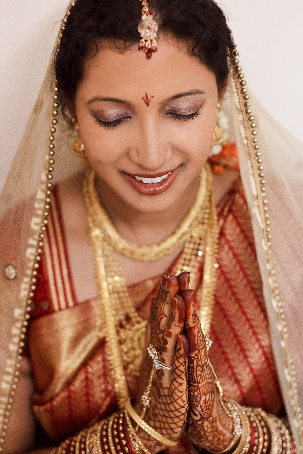 Hindu Wedding Photographer Berlin: Strahlende Braut in Gebetsposition mit aufwendigem Henna Mehndi für die hinduistische Hochzeitszeremonie