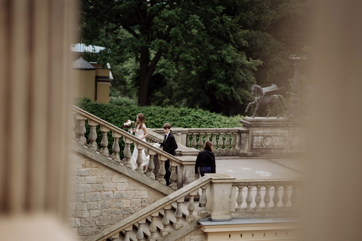 Heiraten in Potsdam: Braut schreitet mit ihrem Bruder die imposante Treppe zum Belvedere auf dem Pfingstberg hinauf