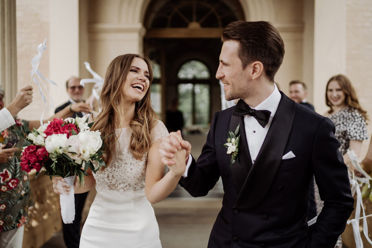 Potsdam Hochzeit: Fröhlicher Auszug aus dem Standesamt mit herzlich lachendem Brautpaar und jubelnden Gästen