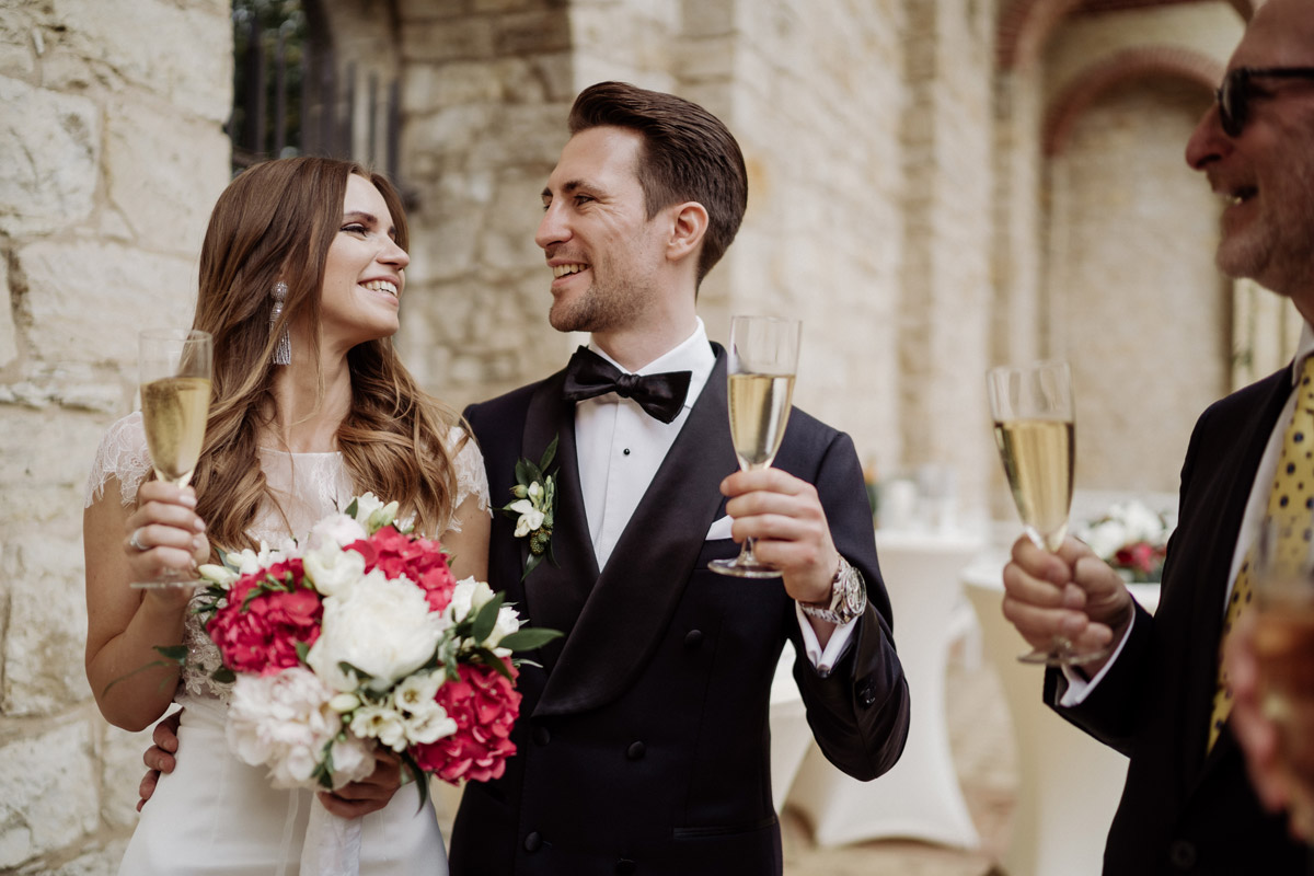 Anstoßen auf das Glück: Brautpaar und Gäste genießen den Sektempfang an den historischen Mauern