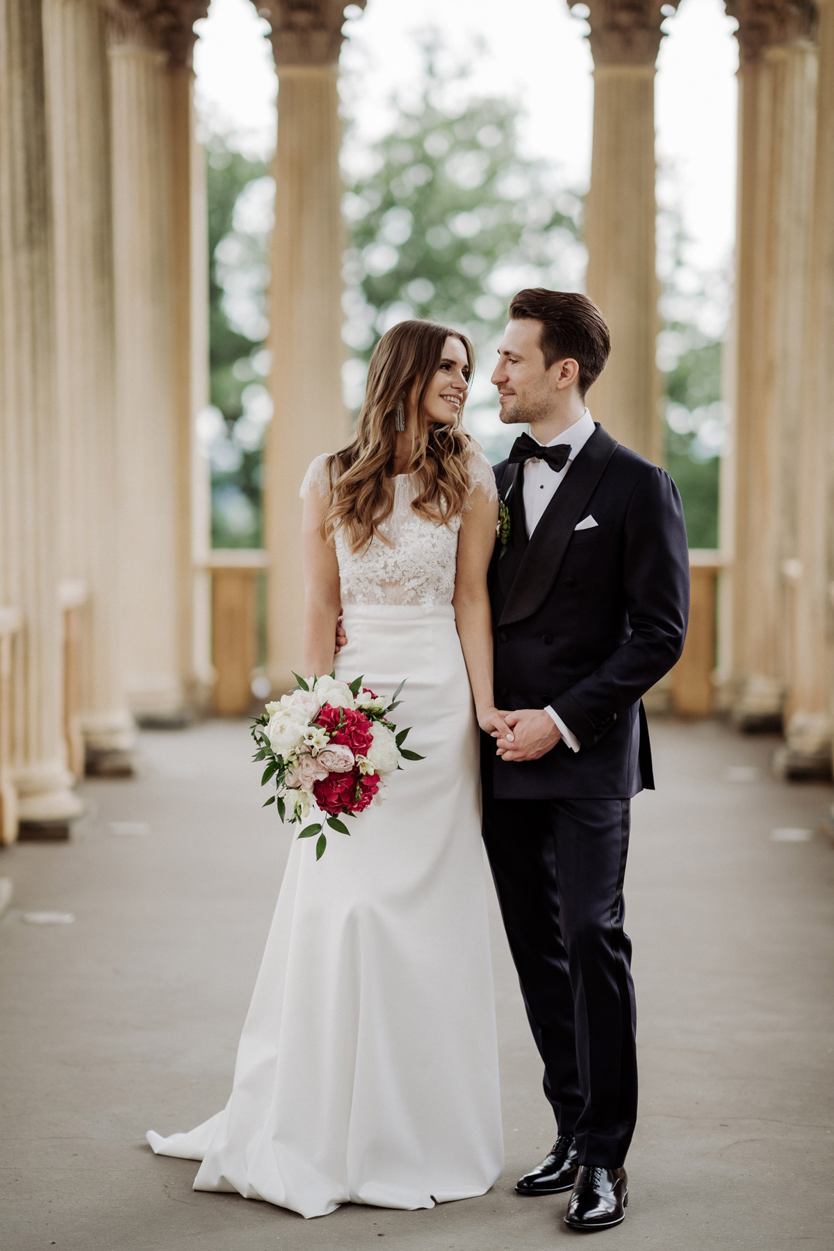 Ganzkörperportrait: Brautpaar schaut sich verliebt im historischen Säulengang an