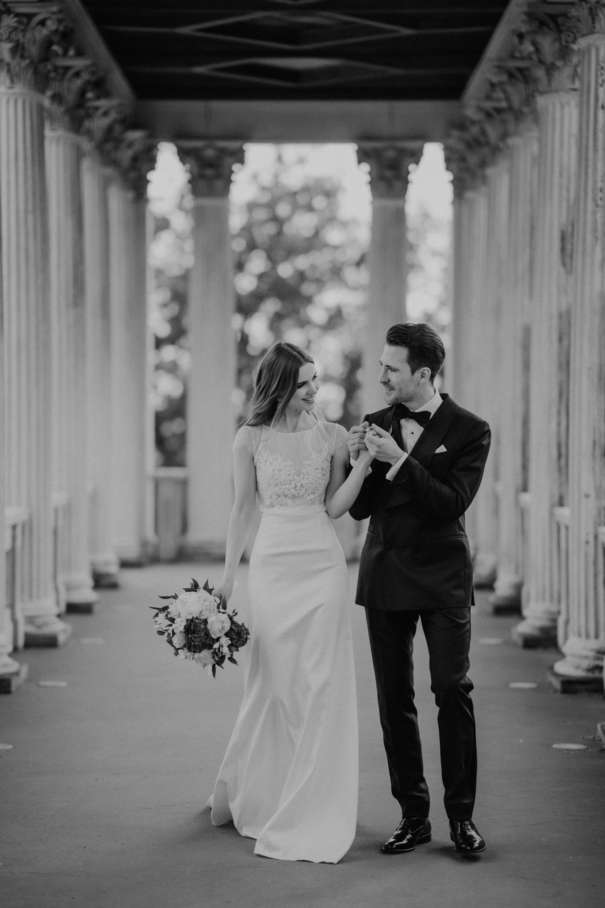 Entspannter Spaziergang: Braut und Bräutigam laufen Hand in Hand durch die Architektur des Belvedere